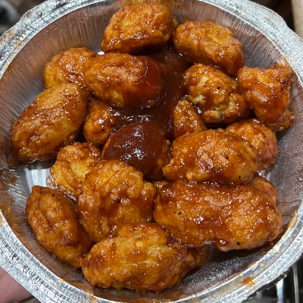 Pizza 72's boneless chicken wings coated in a shiny, dark brown sauce, served in a foil container.