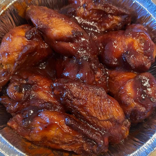 Close-up of several BBQ chicken wings in a foil container from Pizza 72.