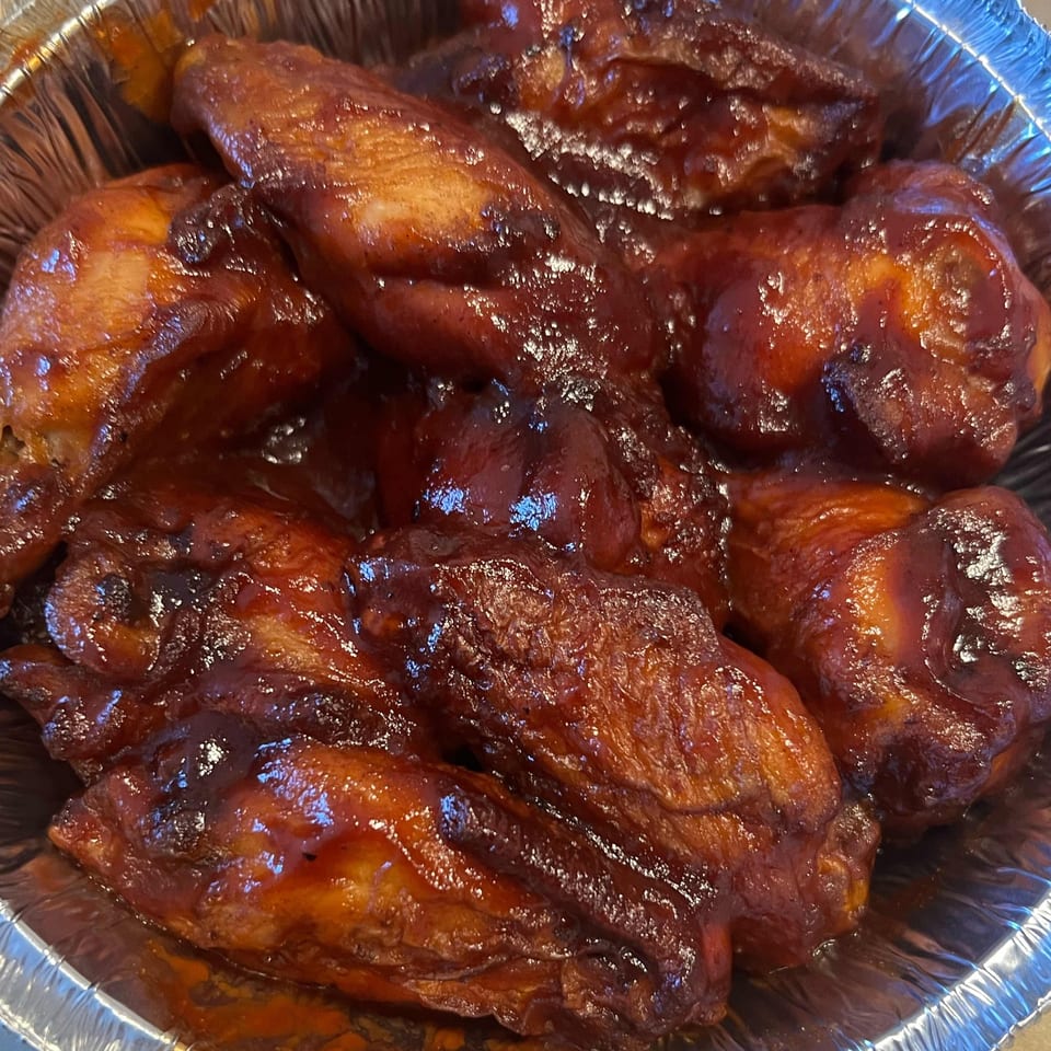 Close-up of several BBQ chicken wings in a foil container from Pizza 72.