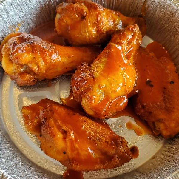 Pizza 72's chicken wings, coated in a glossy orange sauce, served in a foil container.