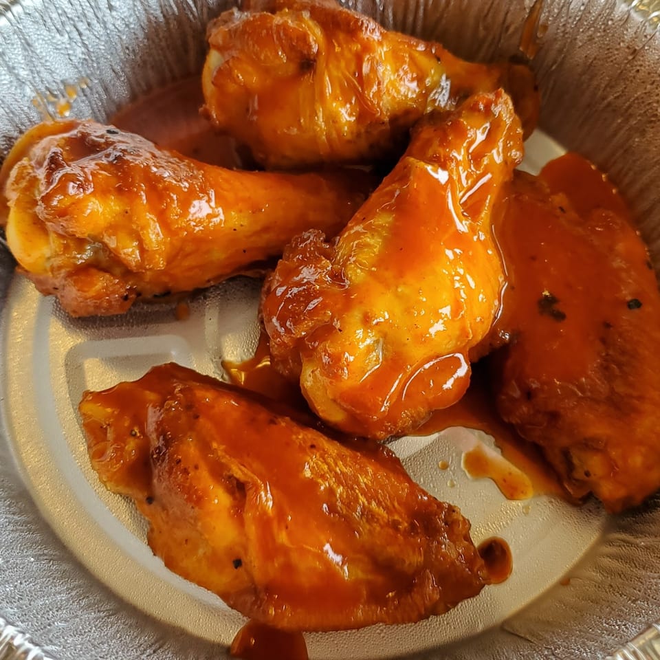 Pizza 72's chicken wings, coated in a glossy orange sauce, served in a foil container.