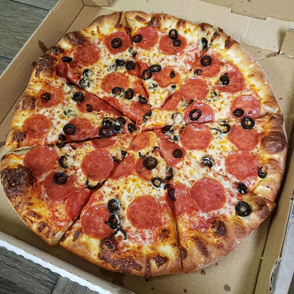 Pizza 72 pepperoni and black olive pizza, sliced in a cardboard box.
