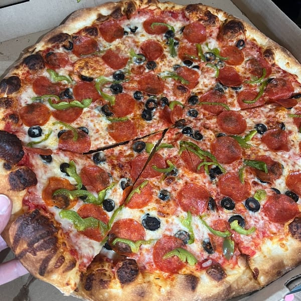 A Pizza 72 pepperoni pizza with black olives and green peppers, with a slice being removed.