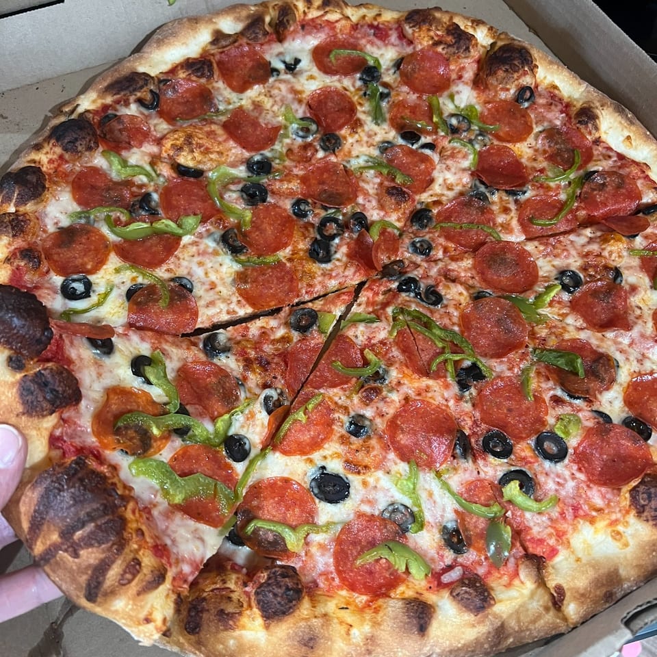 A Pizza 72 pepperoni pizza with black olives and green peppers, with a slice being removed.